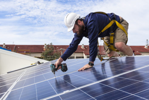 Solar technician fixing in solar panels with a drill