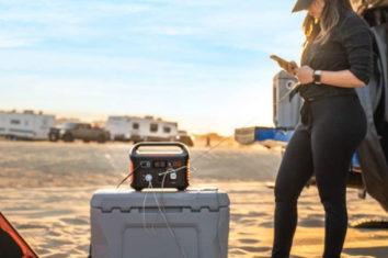 a woman on the beach using a solar generator to charge her phone