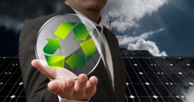 man holding a recycling logo in front of solar panels