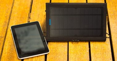portable solar charger sitting on wooden surface next to tablet
