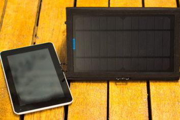 portable solar charger sitting on wooden surface next to tablet